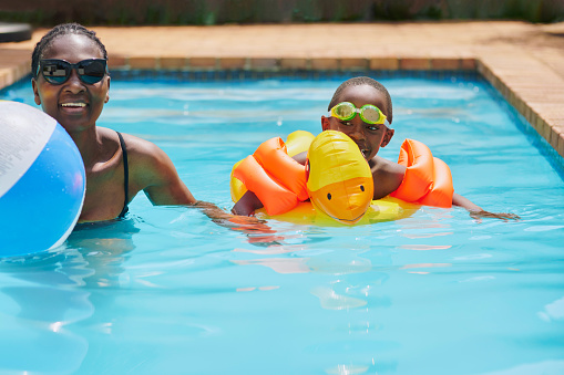 Black family, pool and swimming of a mother learning her child how to swim outdoor. Summer holiday, water and backyard lesson with mama support, love and care for kid on holiday with happiness