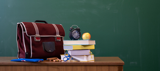 Welcome back to school background - Green blackboard, school bag, textbooks and apple on teacher's desk