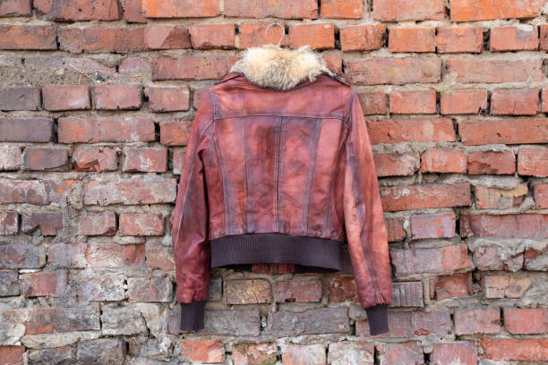 красный мех кожа зимняя женская куртка висит на вешалке на кирпичной старой стене на открытом воздухе во время , женская одежда - brick red wool heat стоковые фото и изображения