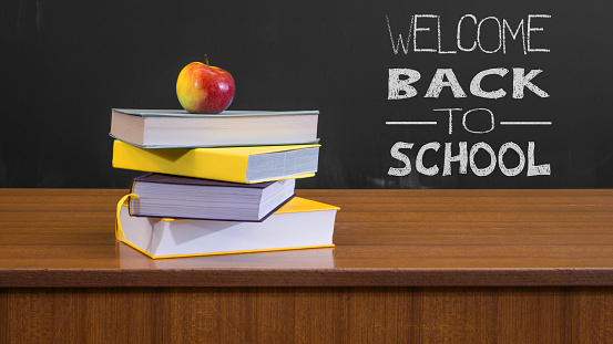 Welcome back to school background - Black blackboard, textbooks and apple on teacher's desk