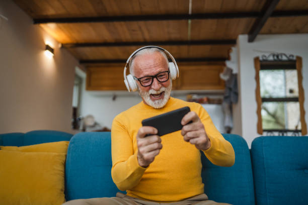 senior old man sit at home play video games on smartphone mobile phone stock photo