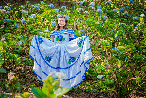Young Nicaraguan woman in traditional folk costume in a field of Milflores, Smiling woman in national folk costume in a field surrounded by flowers. Nicaraguan national folk costume