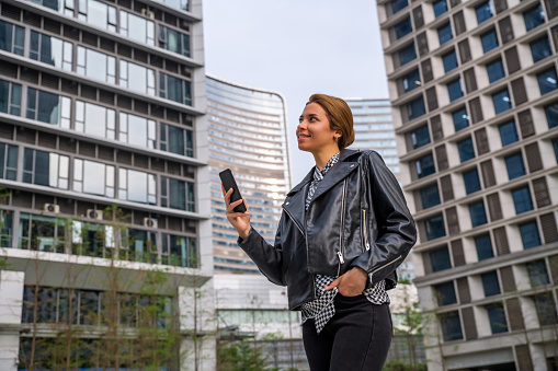 Business woman holding smartphone and looking away outdoors