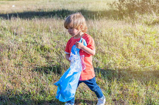 Beautiful Little Boy Collecting Garbage In The Field. Concept Of Education, Caring For The Planet And The Environment