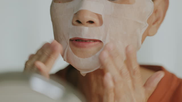 Senior adult woman taking herself with facial mask and massaging face.