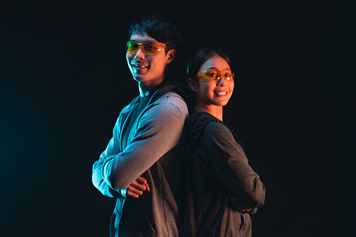 asian cheerful confident couple male and female wearing smart glasses standing together back to back casual look at camera wearing sport active cloth studio shot on dark background