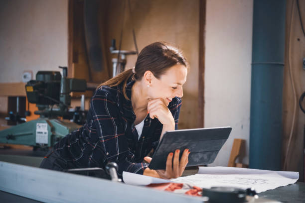 istock Female Carpenter In Garage Workshop Looking At Design On Digital Tablet 1476135499