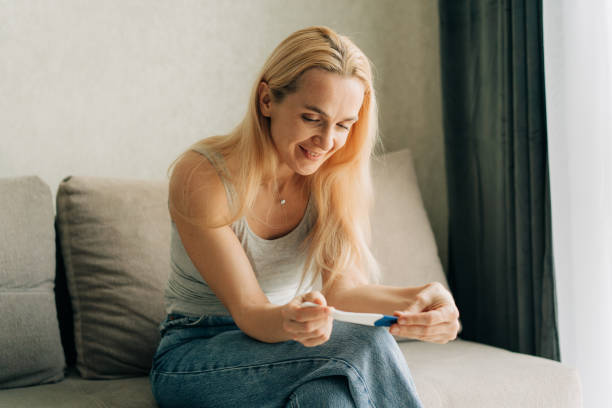 istock Happy smiling woman holding pregnancy test while sitting on sofa at home. 1476136596