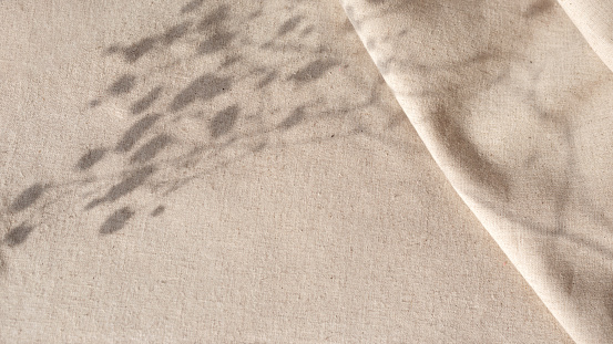 Aesthetic natural minimalistic background, elegant sunlight floral shadows on a neutral beige linen texture pleated tablecloth, background with copy space
