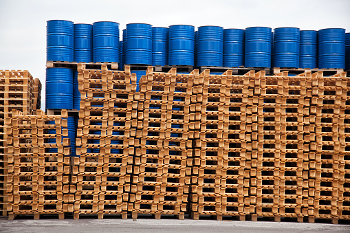 large stack of new euro paletes and blue barrels at factory warehouse
