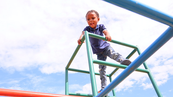 Young black African boy playing on monkey bars in a park