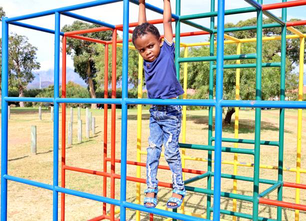istock Young black African boy playing on monkey bars in a park 1476141416