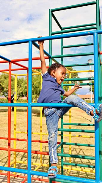 istock Young black African boy playing on monkey bars in a park 1476141420