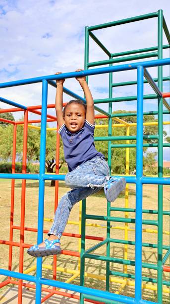 istock Young black African boy playing on monkey bars in a park 1476141421