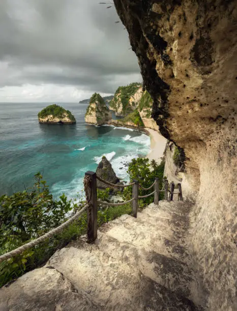 Stairs leading down to the scenic cliffs of Diamond Beach with turquoise water and palm trees surrounding white sand beach and rain clouds gathering a over.
