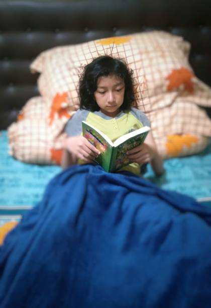 istock Kid is reading a book in her bedroom. 1476144484
