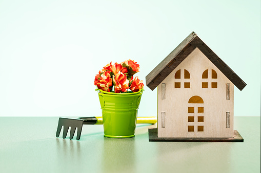 Model of a wooden house, gardening tools and watering can on green background. Gardening concept.