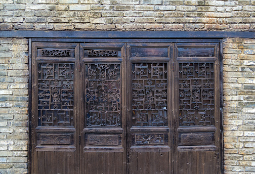 Ancient classic wooden door with typical Chinese architecture style pattern and woodcarving against brick wall