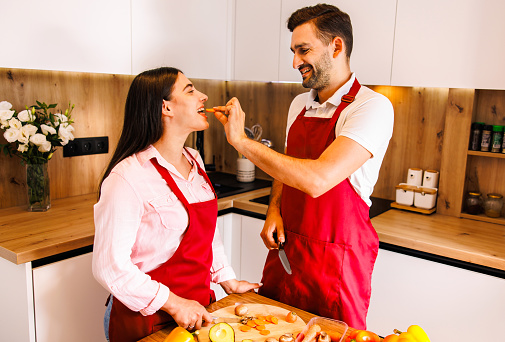 Young cheerful multi-ethnic couple preparing pasta together at their modern kitchen, having fun. High quality photo