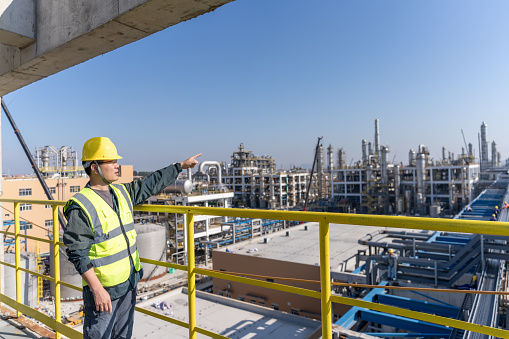 A male engineer points to a chemical plant under construction in the distance
