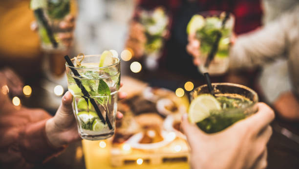 des amis portent un toast à des boissons mojito au pub à cocktails chic speakeasy - concept de style de vie alimentaire et de boissons avec des gens qui s’amusent à encourager l’happy hour au bar - filtre chaud avec accent sur le verre gauche - mojito photos et images de collection