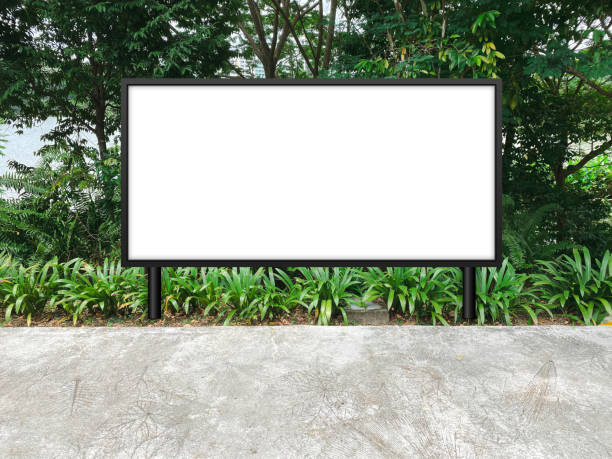 istock Large horizontal blank advertising poster billboard mockup, framed by trees and plants, lush. Straight digital light box display screen for OOH media. Out of home template beside pedestrian path 1476161752