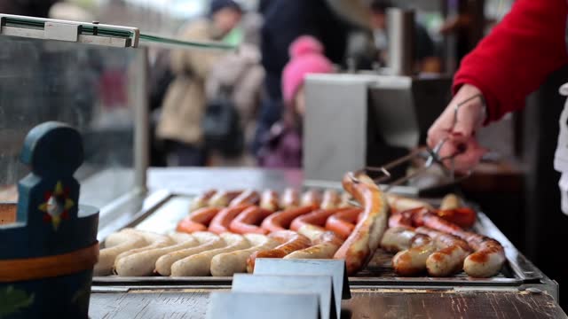 A staff member of a hot dog stand turns German sausages on the cooking grate to be grilled