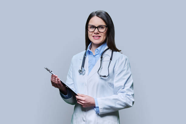 istock Young friendly woman doctor with clipboard on light gray studio background 1476167629