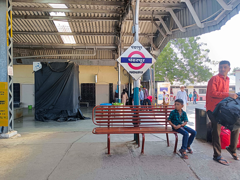 Pandharpur, India- 30th October 2022; An Indian railway platform under a gray-colored shelter. There are a few passengers sitting on the benches, some carrying bags, and others waiting for the train.