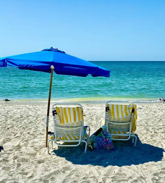 istock Beach scene with yellow striped chairs and blue umbrella 1476170569