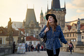 Female traveller tourist on the Charles Bridge in Prague, Czezh Repubic. Stylish beautiful young woman earing black hat. Elegant retro lady fine art portrait.