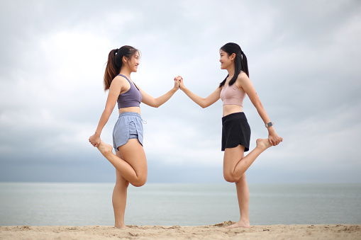 Two Asian young women are doing light stretching exercise together at the beach