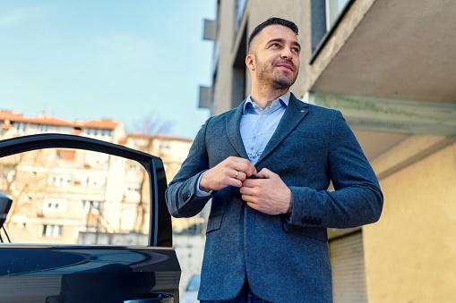 Businessman gets out of the car and buttons his jacket.