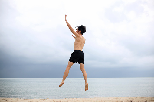 An Asian young man is jumping of joy at the beach