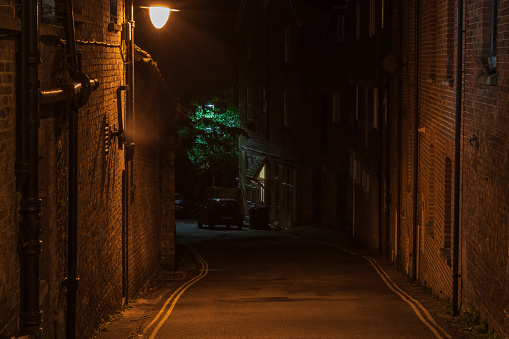 A single dim streetlight illuminates the view down the empty narrow mysterious old town stree