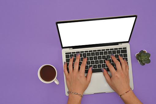 Top view of man's hands painted nails using Empty white screen of laptop computer on the purple background.