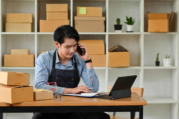 istock Asian man small business owner using mobile and tablet checking order, Entrepreneur seller holding cell phone device preparing retail package postal shipping order in warehouse. 1476182888
