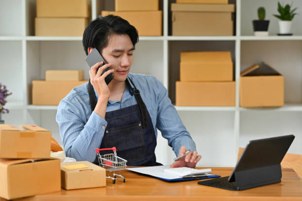 istock Asian man small business owner using mobile and tablet checking order, Entrepreneur seller holding cell phone device preparing retail package postal shipping order in warehouse. 1476183065