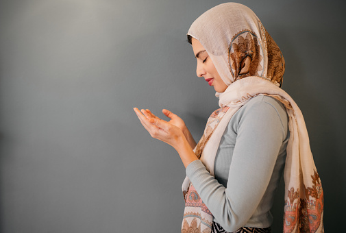 Side view portrait of a young Muslim woman praying with her eyes closed.