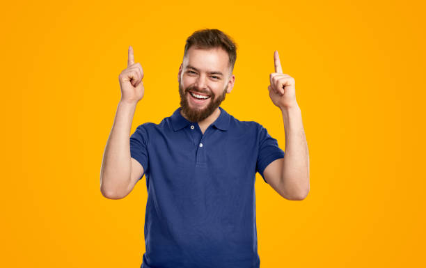 istock Cheerful young man gesturing forefingers up and smiling at camera 1476194989