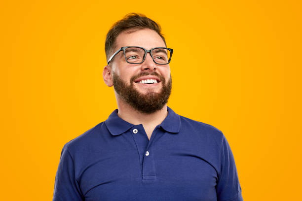 Happy young man smiling and looking away in yellow studio stock photo