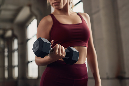 Crop unrecognizable fit female in fitness clothes doing bicep curls with dumbbell during functional workout in gym