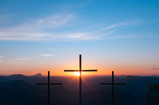 Three crosses on top of a mountain with the sunset in the background representing the crucifixion and resurrection of Jesus Christ.