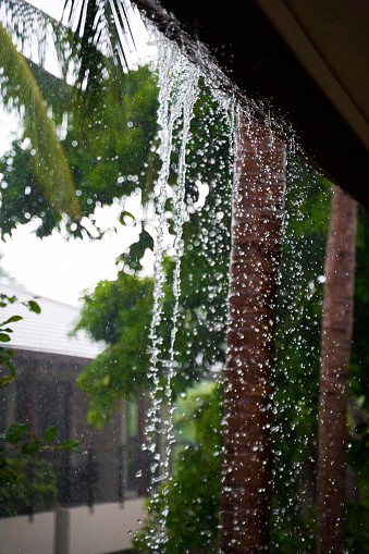 Water falls from the roof breaking the drain during a heavy tropical downpour.