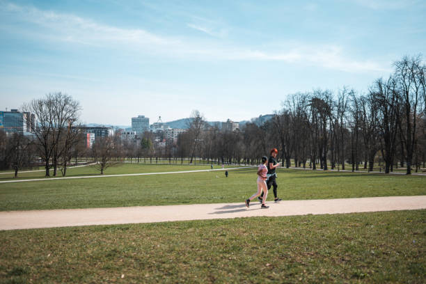 Indian female and Asian male running in a public park. Joggin together on a lovely sunny day wearing sports clothing.
