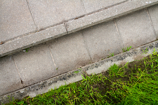 The system of drainage of melt water, rain streams and floods. Close up of concrete tiles and grass.