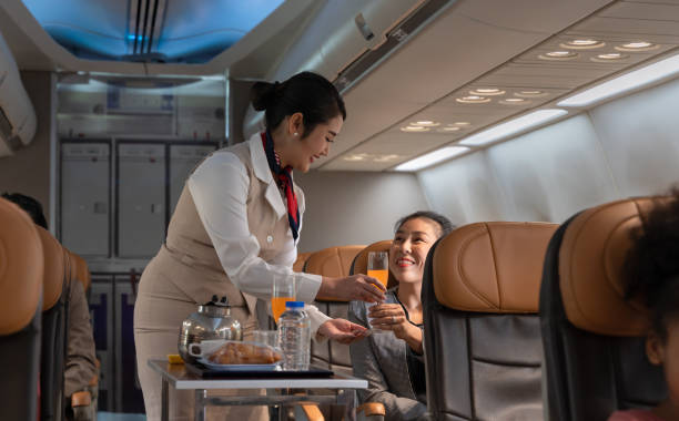 Airplane flight attendant serving orange juice to female passenger in cabin. Air hostess or cabin crew working in airplane. Female flight attendant serving orange juice to businesswoman passenger on board. Airline transportation and tourism concept. airplane food stock pictures, royalty-free photos & images