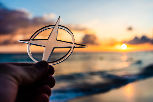 Hand holding a compass like transparent object on the beach at sunset