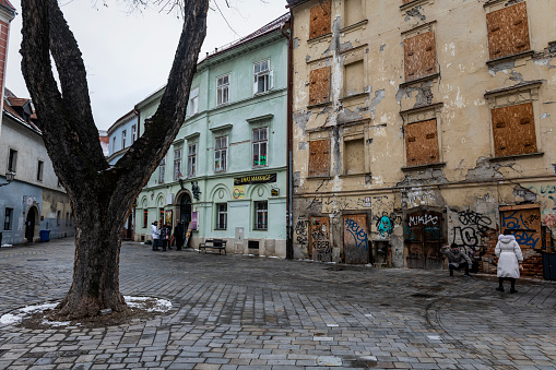 Bratislava, Slovakia - January 28, 2023: A tourist crouches and poses for a picture in front of a boarded-up building in the old town area of Bratislava.