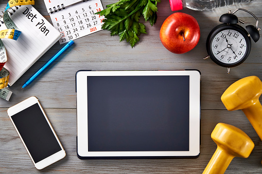 Top view of Clock, notepad with pen, digital tablet, dumbbells, smartphone, tape measure, water bottle, apple and smart watch on a table